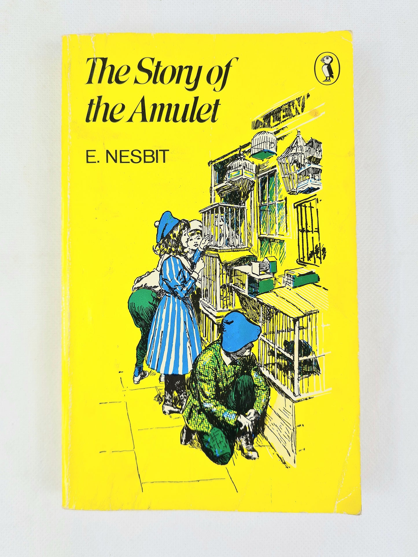 Book cover of 'The Story of the Amulet' by E. Nesbit with an illustration of two children and a birdcage.