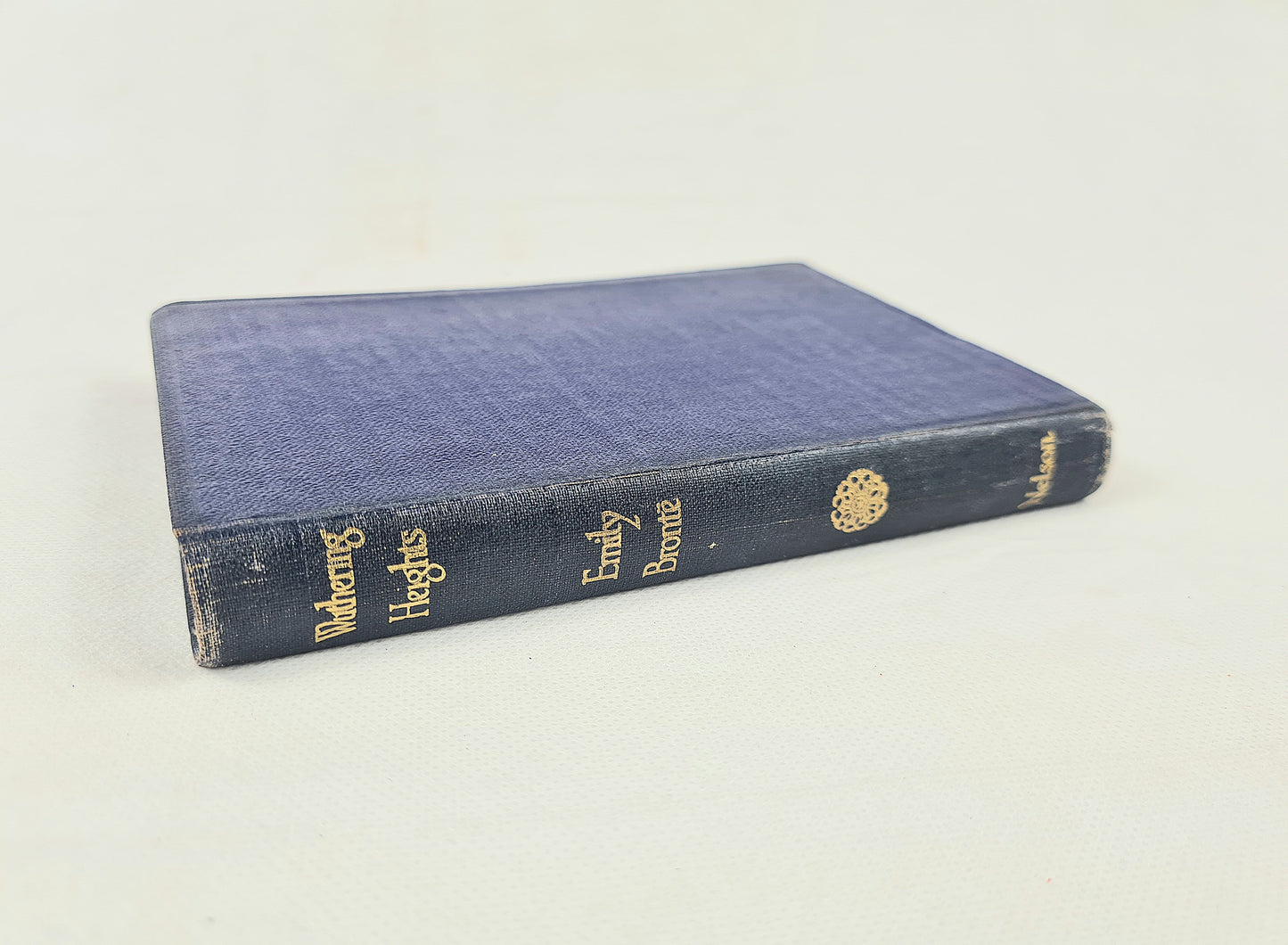 A vintage hardcover book titled 'Wandering Heights' by Emily Bronte, featuring a textured navy blue cloth cover with gold-foiled lettering on the spine, photographed on a light off-white background.