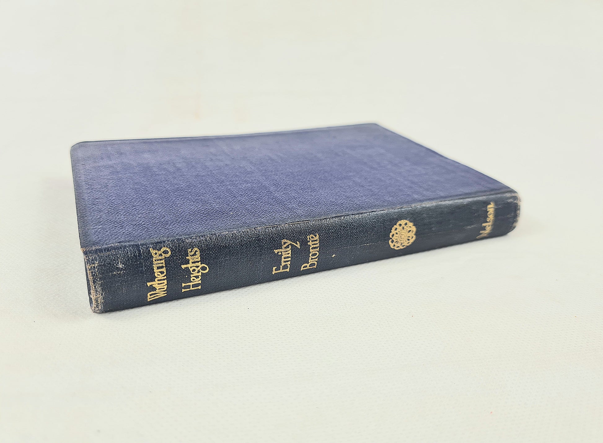 A vintage hardcover book titled 'Wandering Heights' by Emily Bronte, featuring a textured navy blue cloth cover with gold-foiled lettering on the spine, photographed on a light off-white background.