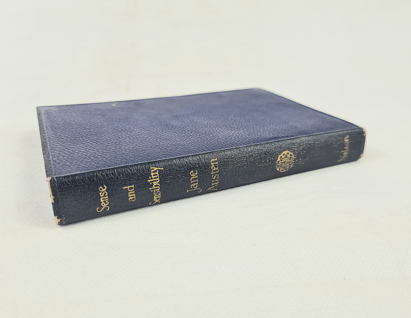 A vintage hardcover book with a textured navy blue leather cover and gold lettering on the spine, photographed on a light off-white background.