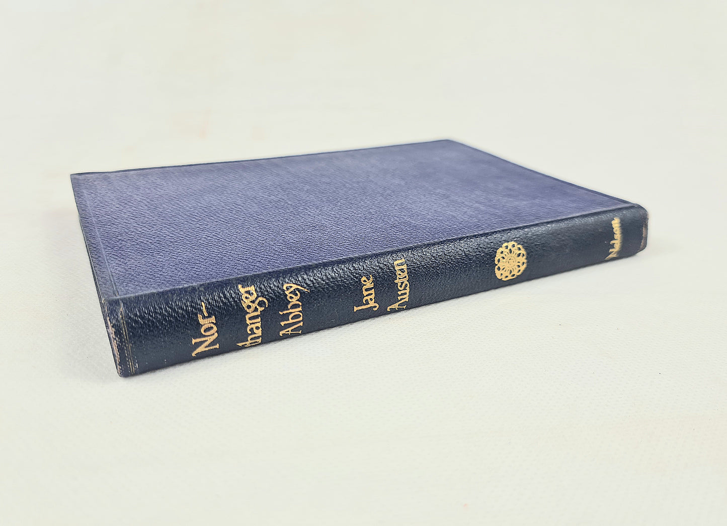A vintage hardcover book titled 'Northanger Abbey by Jane Austen with a textured navy blue leather cover and gold embossed lettering, photographed on a plain off-white background.