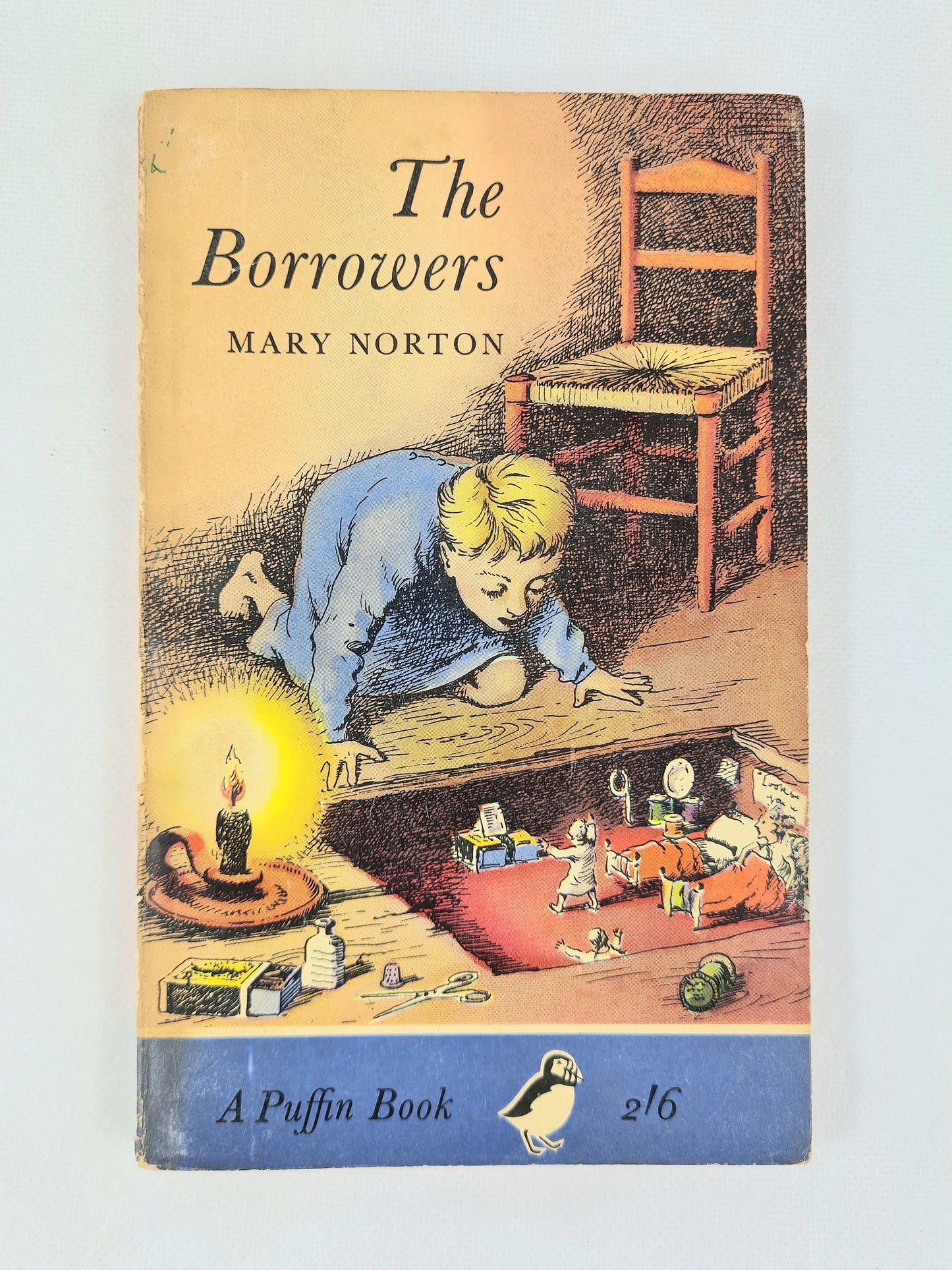 Vintage paperback book cover of 'The Borrowers' by Mary Norton, published by Puffin. The cover features an illustration of a young boy in a blue pajama lying on the floor looking into a dark hollow beneath where children are playing.