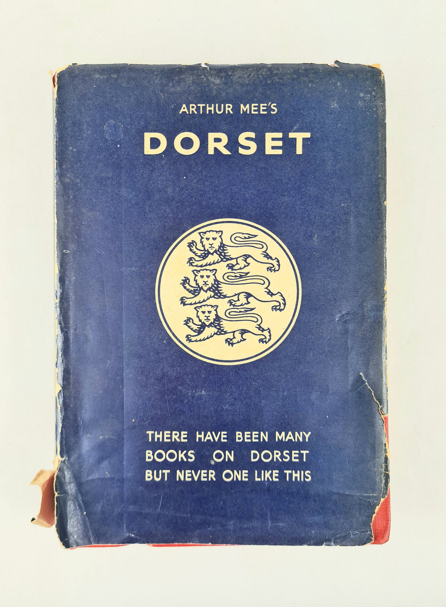 A vintage hardcover book titled 'Arthur Mee's Dorset' with a dark blue cover, cream-colored text and lion emblem, and worn edges, photographed against a plain light background.