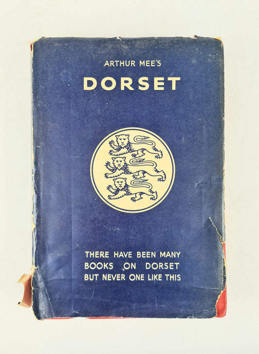 A vintage hardcover book titled 'Arthur Mee's Dorset' with a dark blue cover, cream-colored text and lion emblem, and worn edges, photographed against a plain light background.