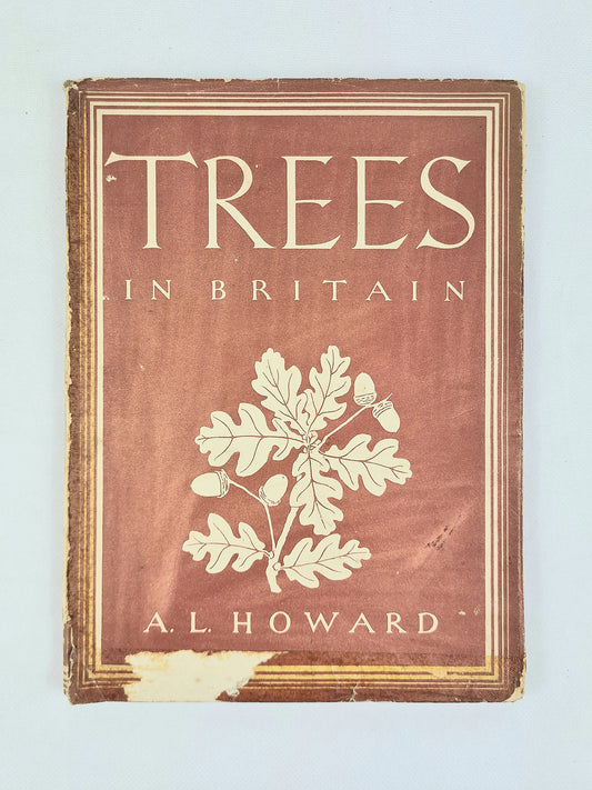 A vintage book titled 'Trees in Britain' by A. Howard, featuring a reddish-brown cover with cream-colored text and an oak leaf illustration, photographed against a light blue background.