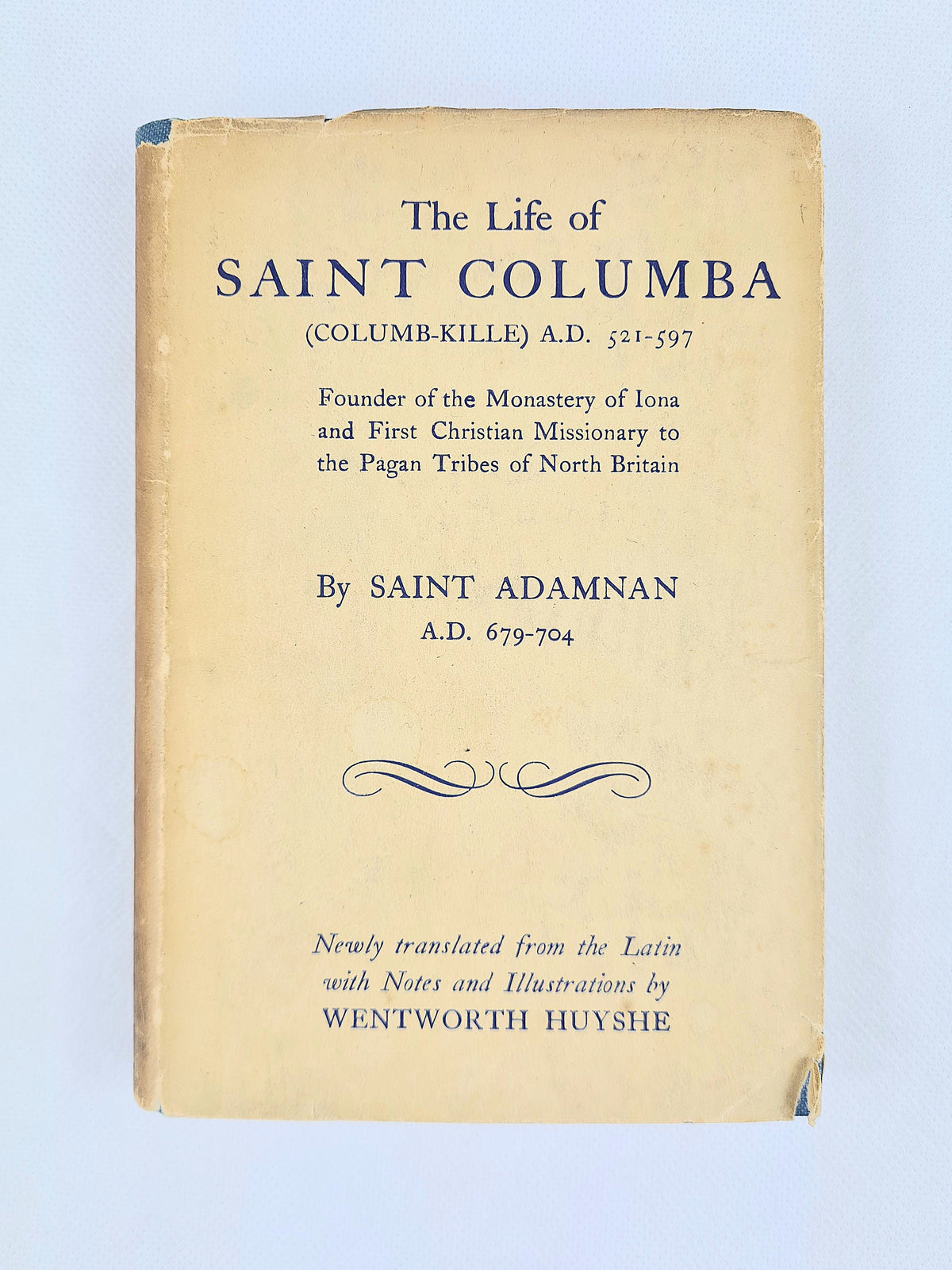 A vintage book cover for 'The Life of Saint Columba' by Saint Adamnan, featuring a warm beige background with dark blue printed text and decorative flourishes, shown against a light blue background.